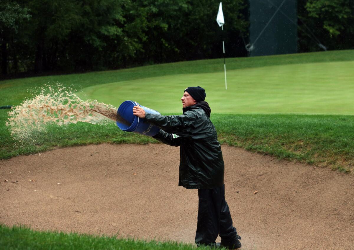 Volunteer Ben Pfeffer removes water from the bunker on the 1st hole during the rain delay on the last round of BMW Championship at Conway Farms Golf Club, in Lake Forest, Ill., on Sunday.