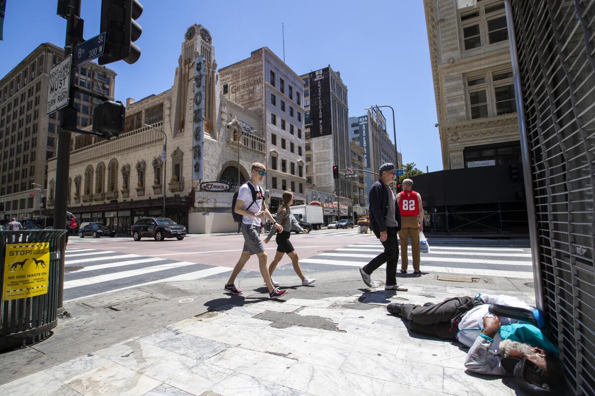 Pedestrians walk past a homeless man on the sidewalk at 8th and Broadway in L.A.