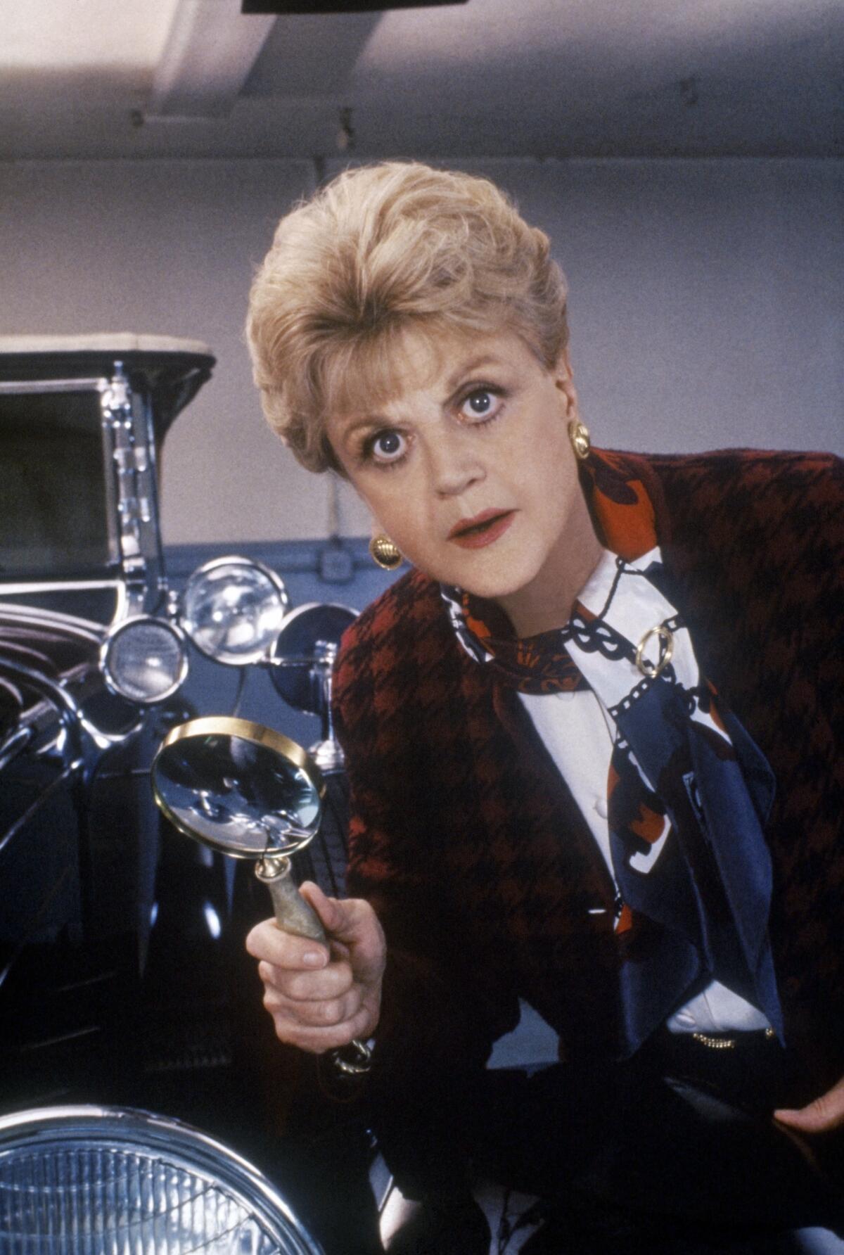 Angela Lansbury holds a magnifying glass in front of an old-fashioned car in a scene from "Murder, She Wrote.” 