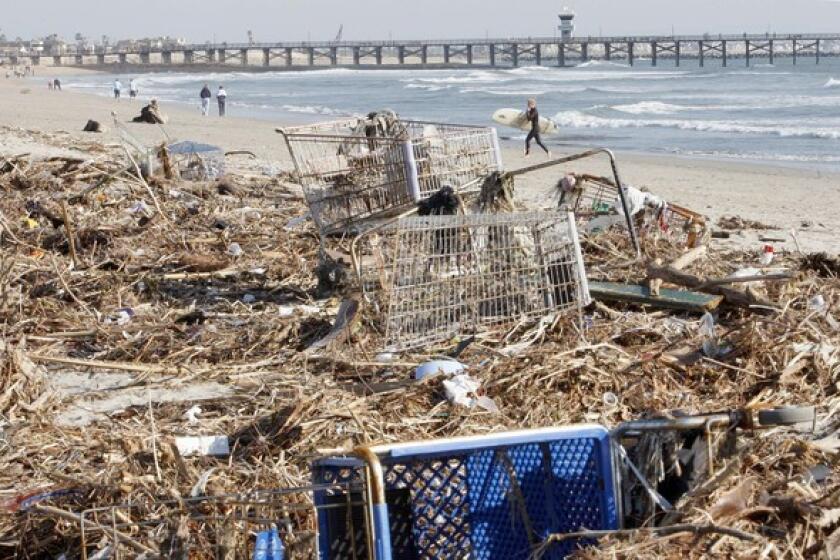 Last week's storms left Southland beaches littered with trash. "It's gross...the water was really murky," said Kelsey Widman, background, who braved the piles of refuse to catch some choice waves at Seal Beach.