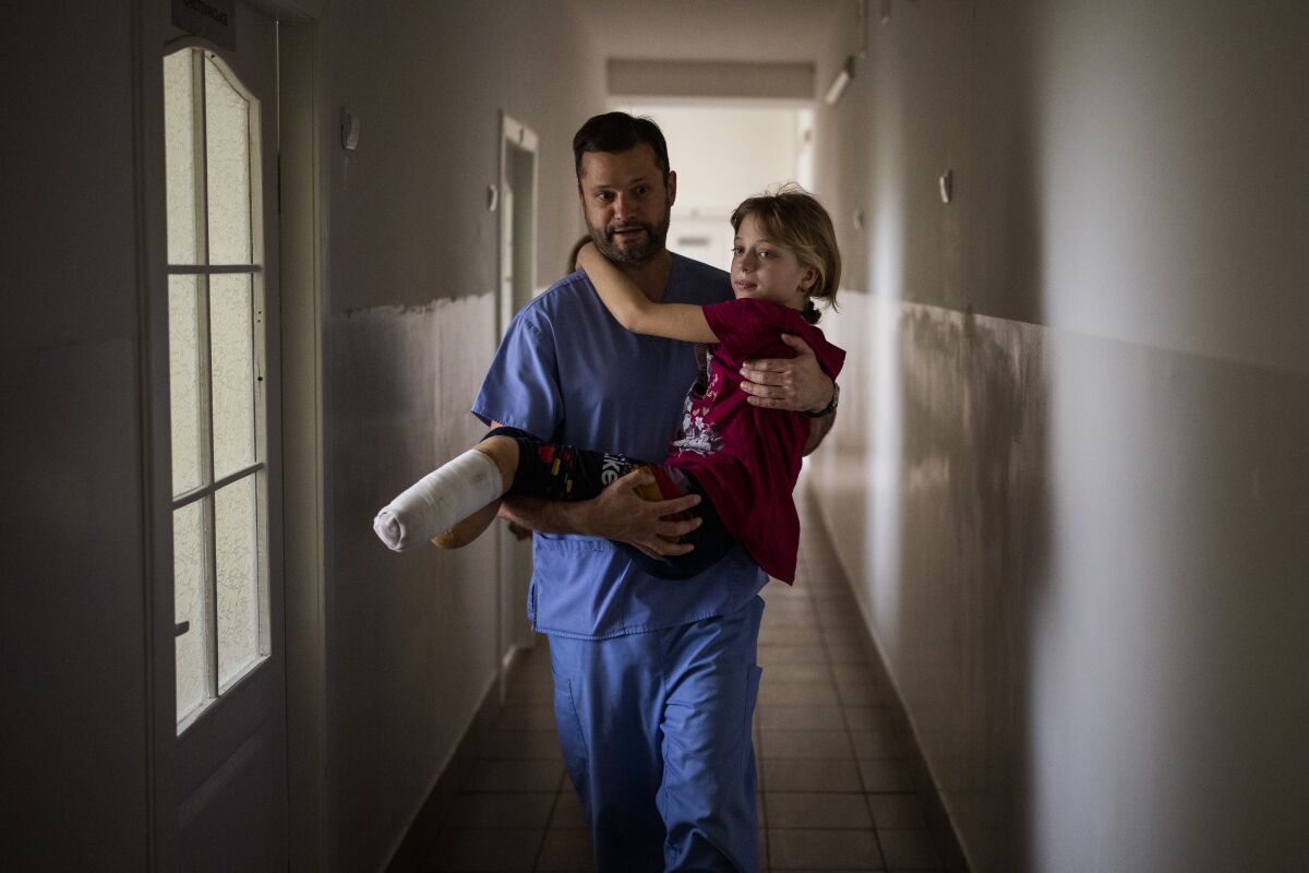 Yana Stepanenko, 11, is carried by a doctor at a public hospital in Lviv, Ukraine, Friday, May 13, 2022. Yana and her mother Natasha, 43, were injured April 8 during shelling at the train station of the eastern city of Kramatorsk where they travelled with Yana's twin brother Yarik from their village near the front line. They were planning to catch an evacuation train heading west and, they hoped, to safety. (AP Photo/Emilio Morenatti)