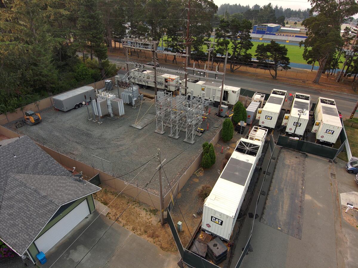 Six large generators the size of trailers on an electric substation next to a high school field