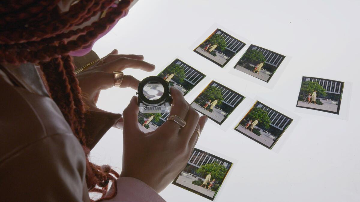 A woman uses a magnifier to look at squares of film negative on a light table