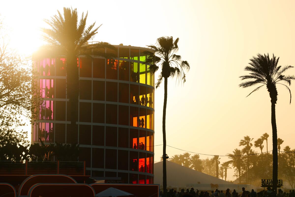 People walk through the multistory Rainbow tower near palm trees.