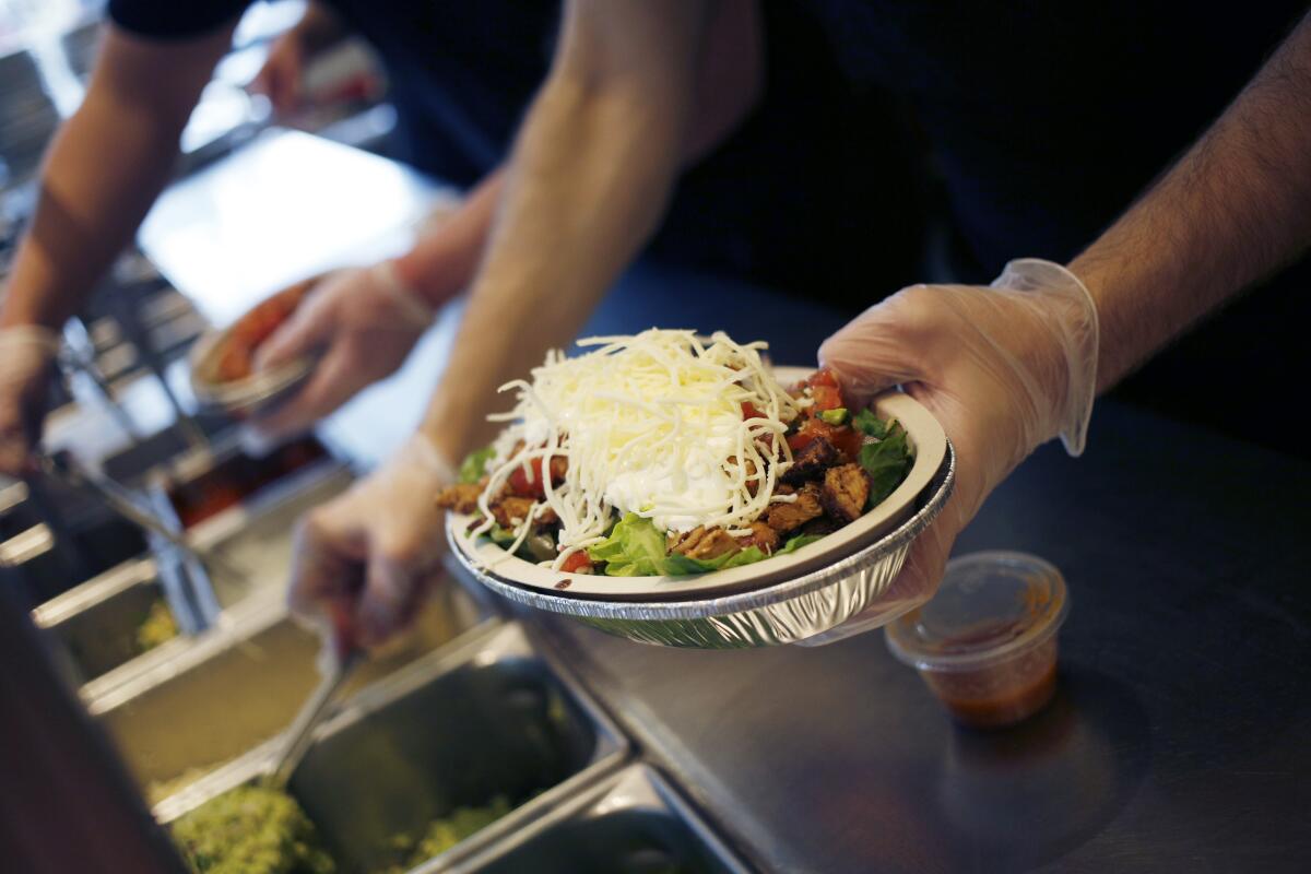 An employee prepares a burrito bowl at a Chipotle. 
