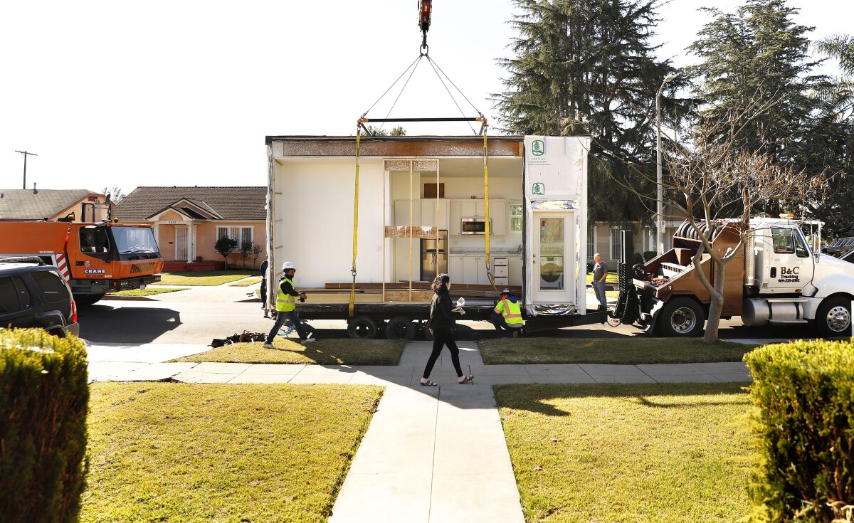 A prefabricated ADU is hoisted from a trailer.