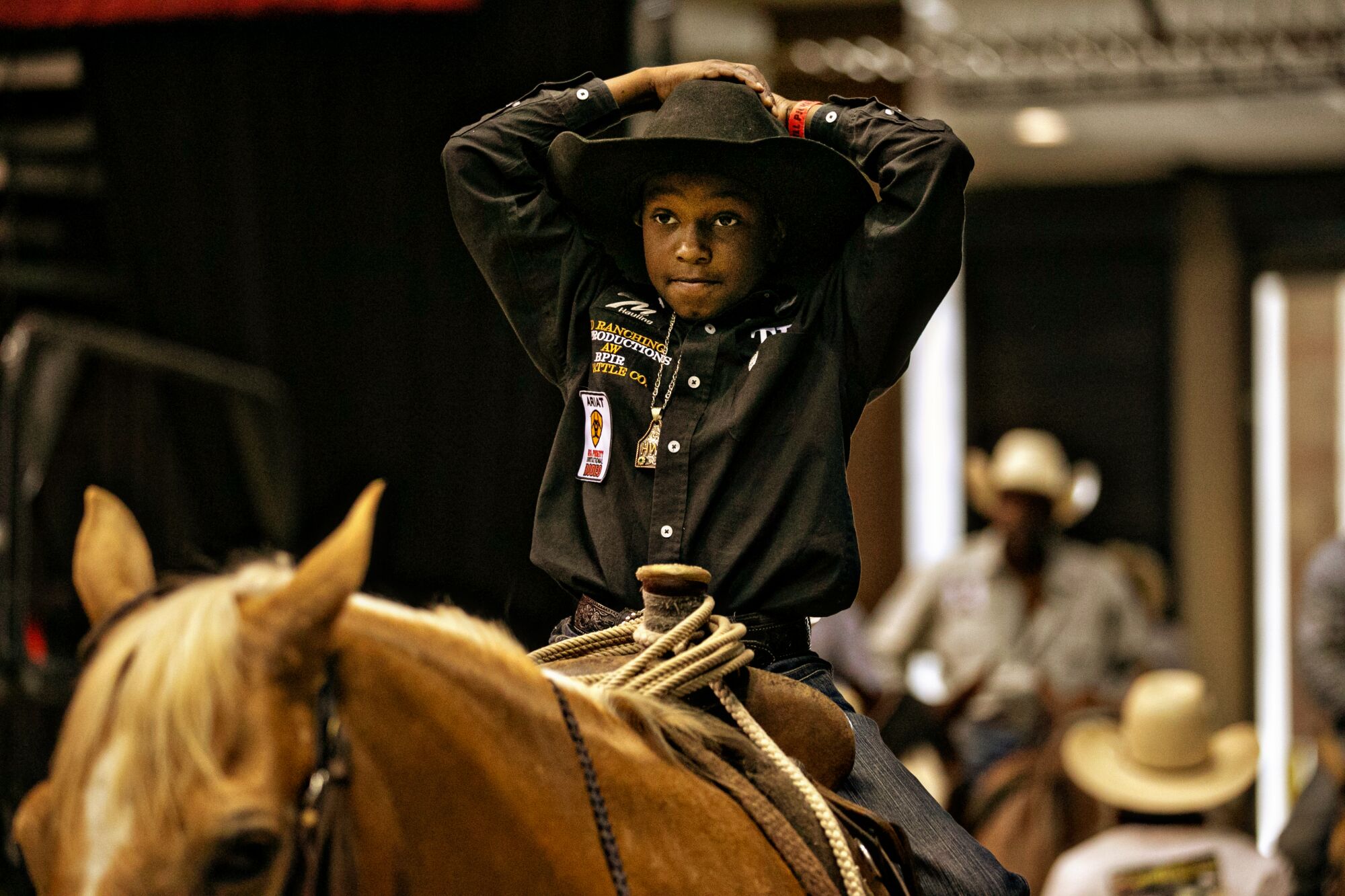 A boy sitting on his horse with his hands on his cowboy hat