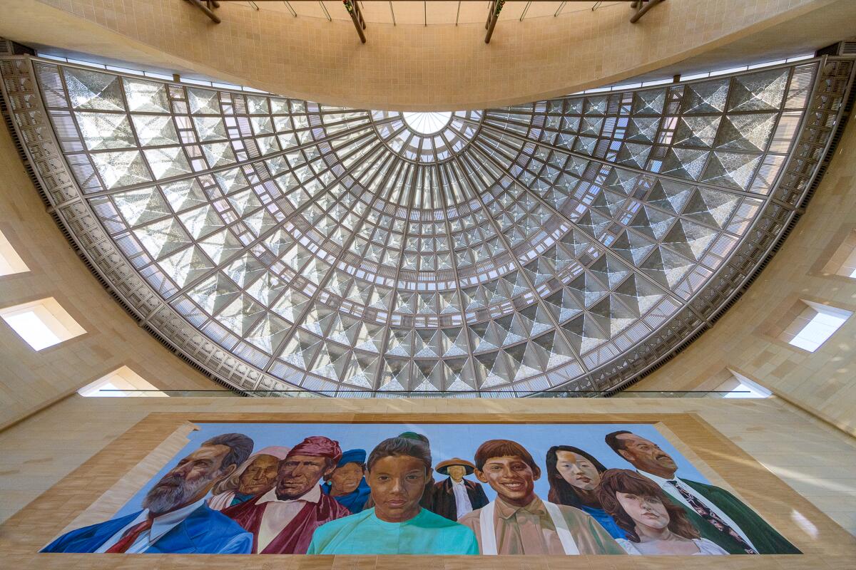 A half-circular skylight of clear glass panels above a mural depicting the diverse faces of Los Angeles.