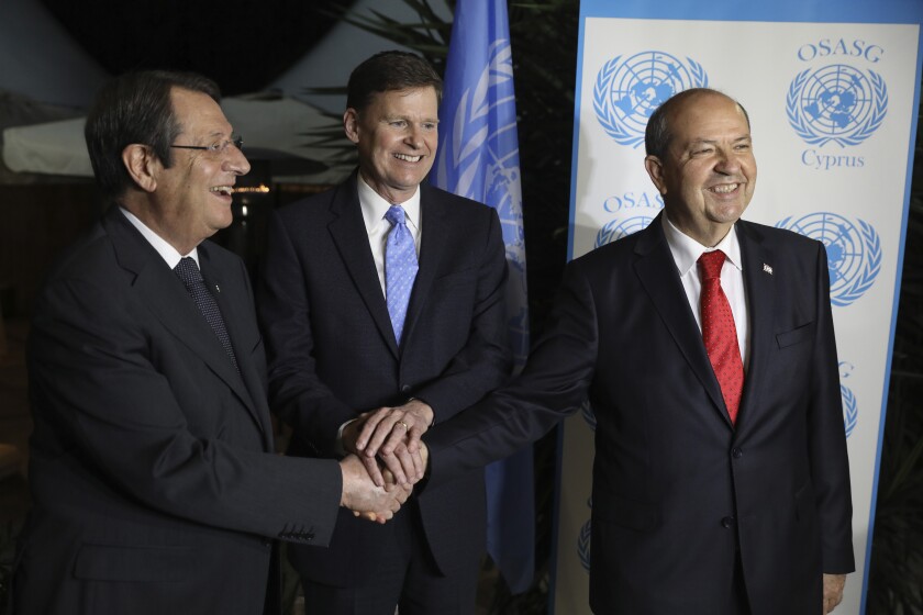 Cyprus' Greek Cypriot President Nicos Anastasiades, left, Ersin Tatar, leader of the breakaway Turkish Cypriots, right, and Colin Stewart, the new head of the United Nations peacekeeping mission on the ethnically divided island nation, shake hands during their meeting in Ledra Palace abandoned hotel inside the U.N. controlled buffer zone that cuts through the capital Nicosia, on Tuesday, Dec. 14, 2021. The meeting is billed primarily as a social event geared toward breaking the ice between the two leaders in the absence of formal talks that have been at a standstill since the last bid to reach a reunification agreement collapsed in the summer of 2017. (Yiannis Kourtoglou/Pool via AP)