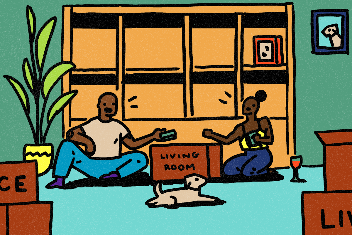 A couple with their dog in front of a bookcase, sitting on the floor and packing things into boxes
