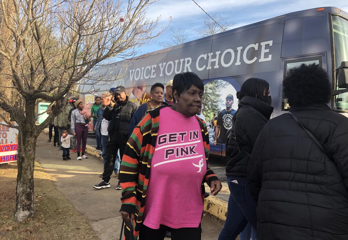 People stand in line next to a bus emblazoned with the words, "Voice your choice." 