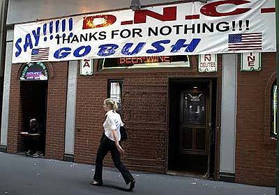 A woman passes a sign critical of the Democratic National Convention at a restaurant across from the Fleet Center. The owner of the pizza parlor has complained of having to close his business during next week's convention.