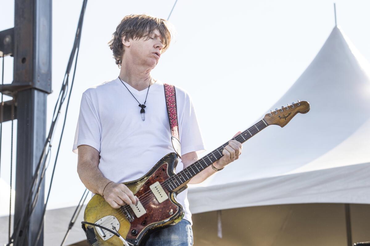 Sonic Youth co-founder Thurston Moore wears a white T-shirt and plays a sunburst guitar with a tortoiseshell pick guard.