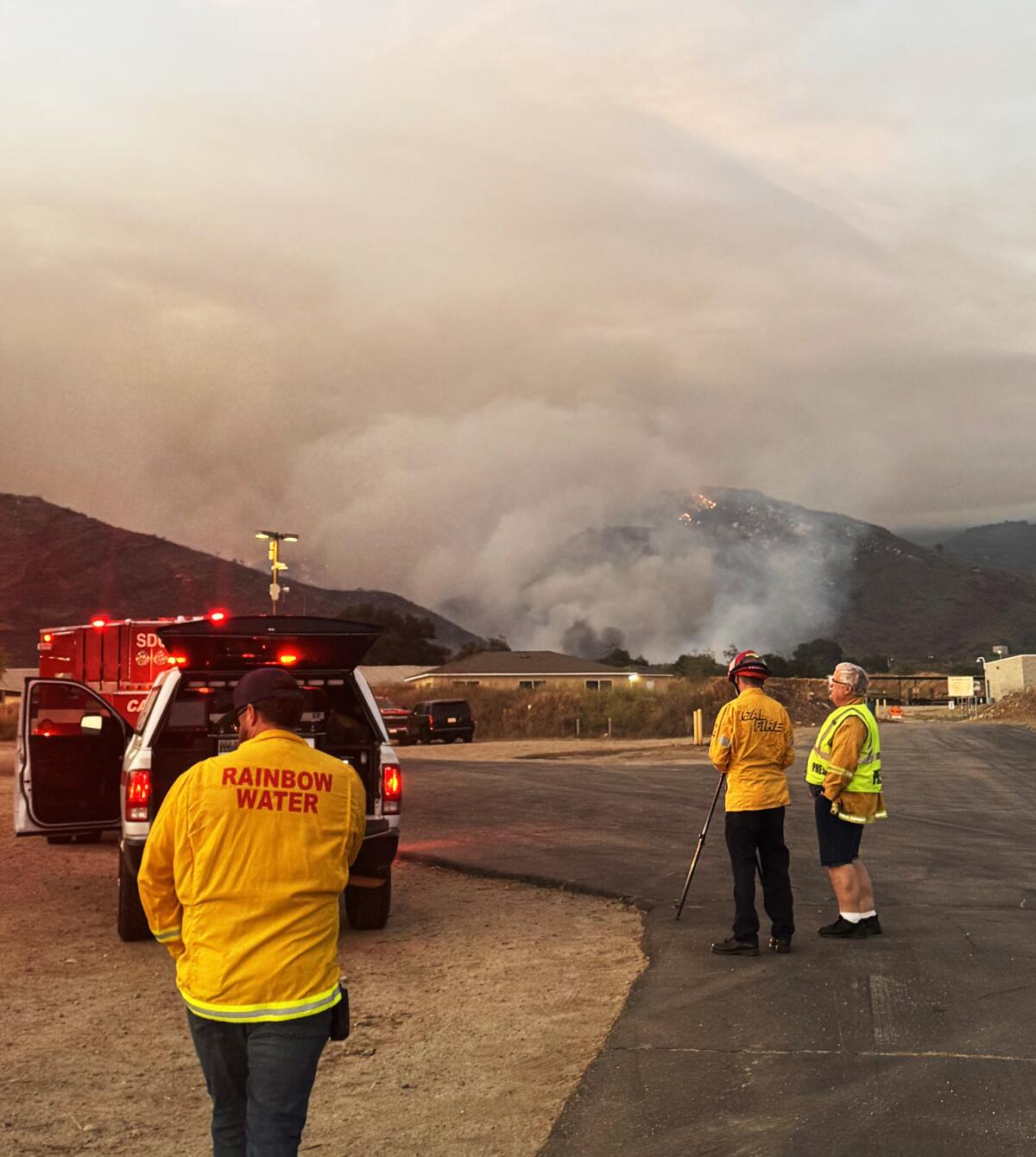 Firefighters watch smoke over hills.
