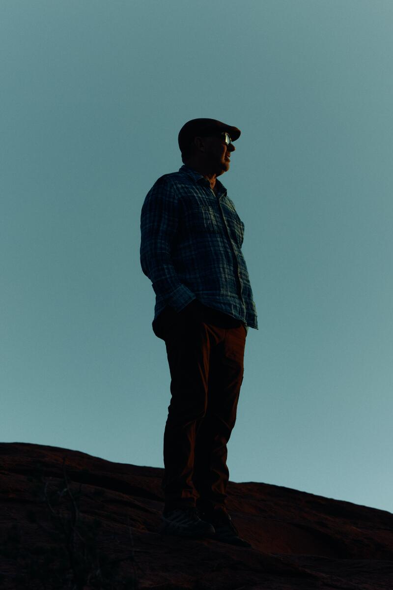 A man stands on a hill watching the sunset.