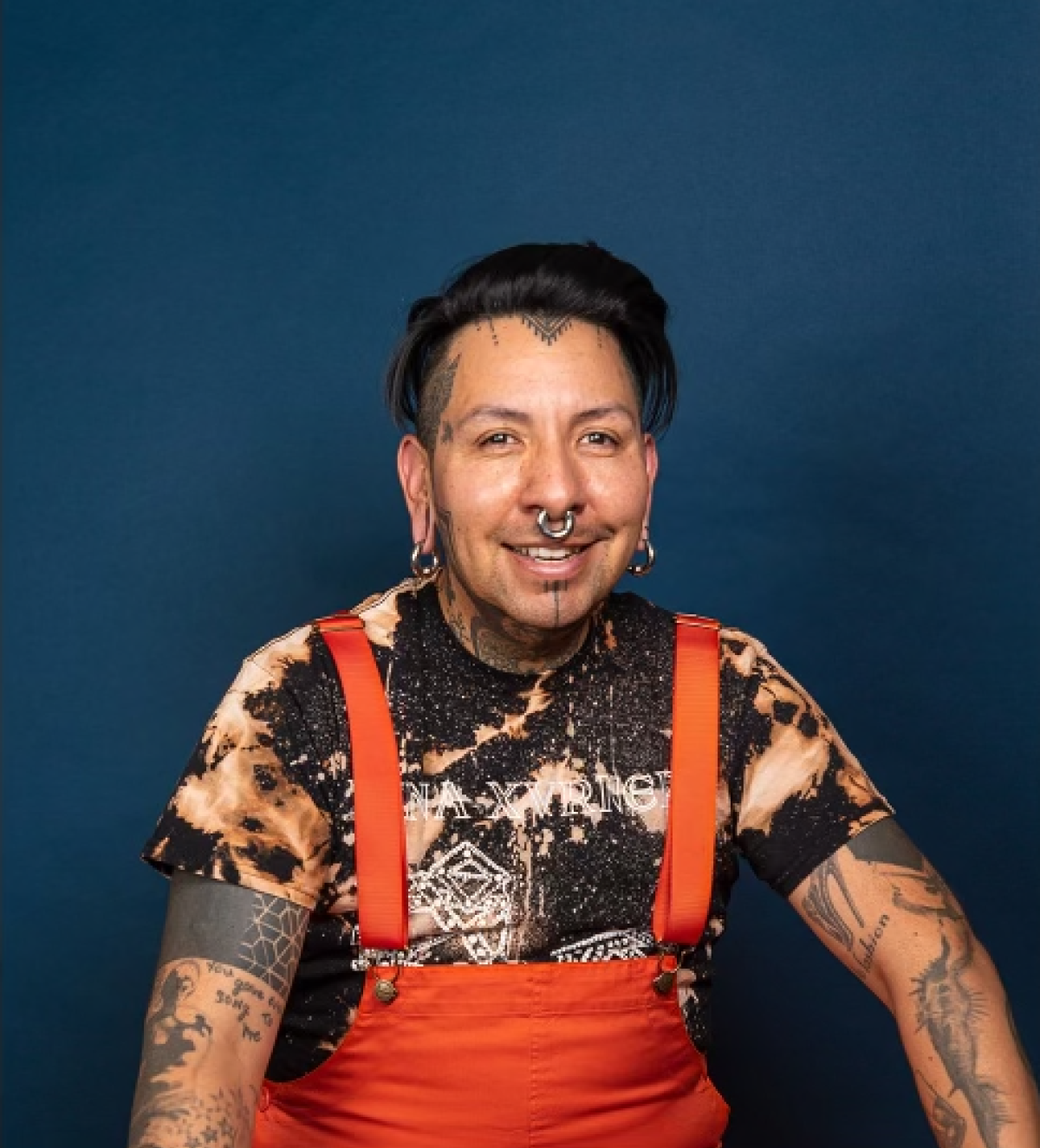 person with septum piercing in orange overalls