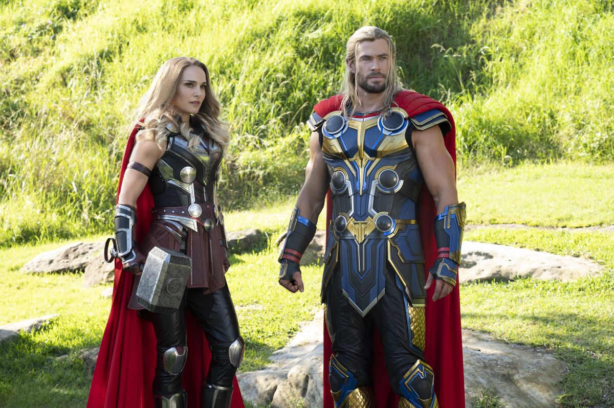 A woman in a superhero costume holding a large hammer and standing next to a man in a matching superhero costume