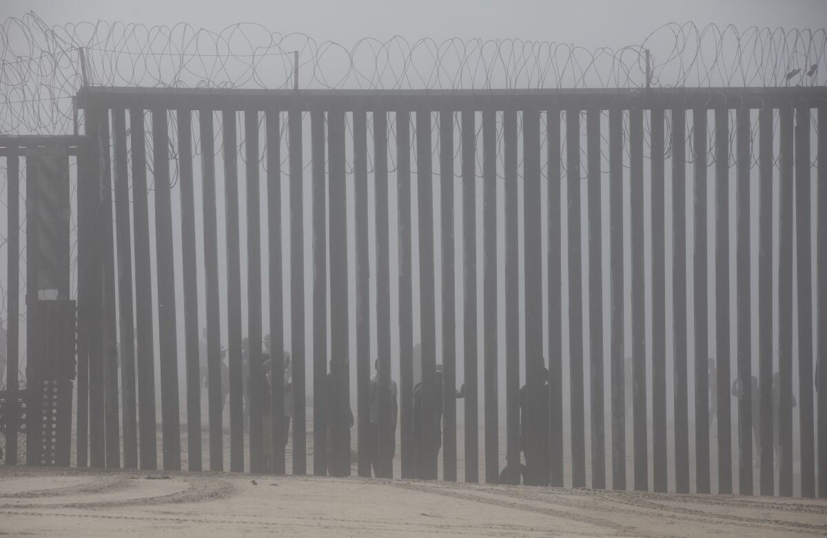 People peer through border fence from Tijuana.