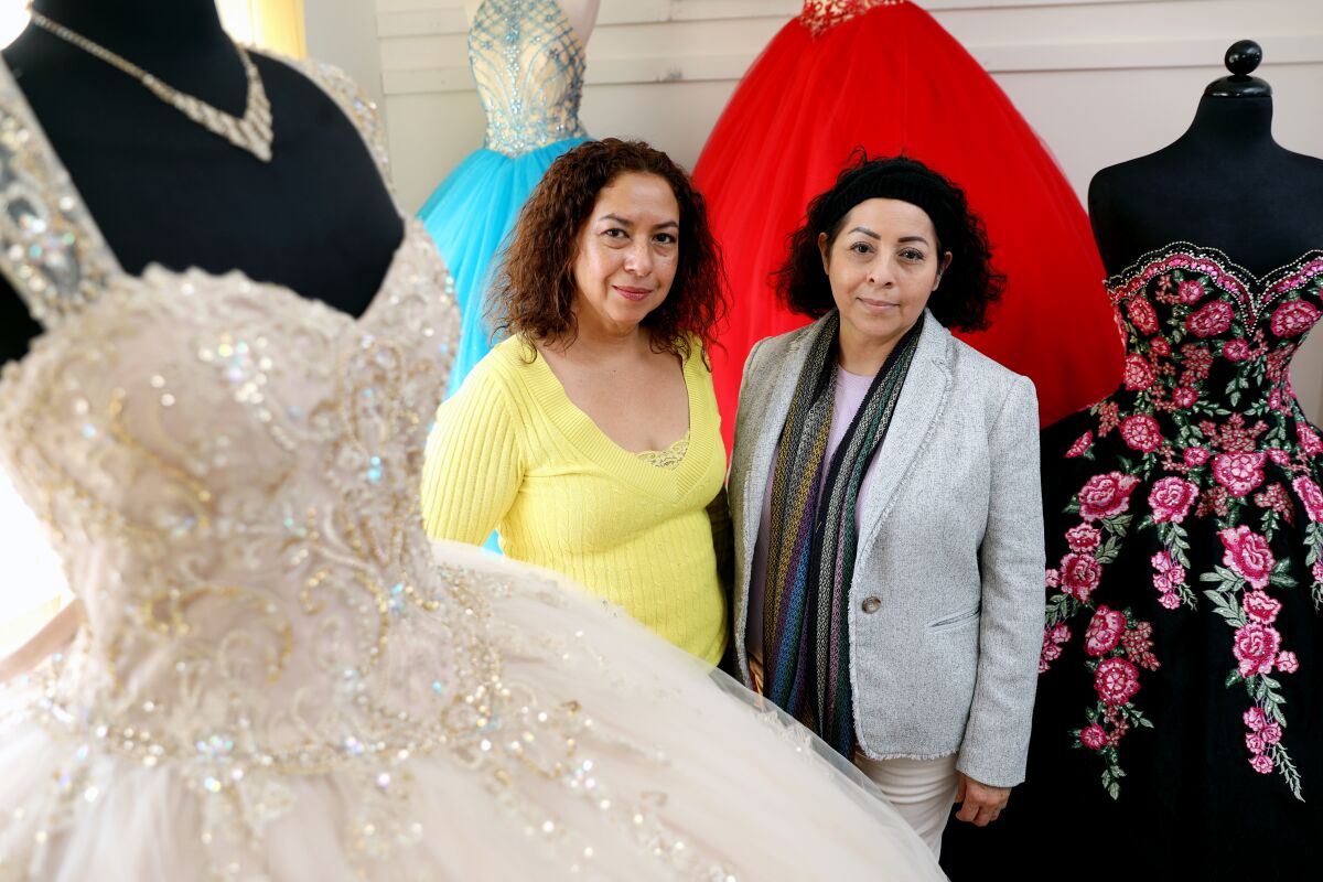 Vicky Cerpas, owner of Creaciones Alejandra photo studio and bridal shop, with sister Lilia Cerpas, owner of Genesis Bridal Boutique, at Genesis Bridal Boutique in Santa Ana. Three sisters, who each have quinceanera shops, had to close their shops after business dried up because of the coronavirus pandemic. They have joined forces to make face masks.