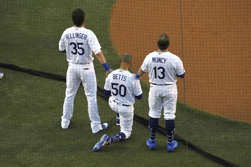 Los Angeles Dodgers' Cody Bellinger, left, and Max Muncy, right, put their hands on Mookie Betts during the national anthem prior to an opening day baseball game Thursday, July 23, 2020, in Los Angeles. (AP Photo/Mark J. Terrill)