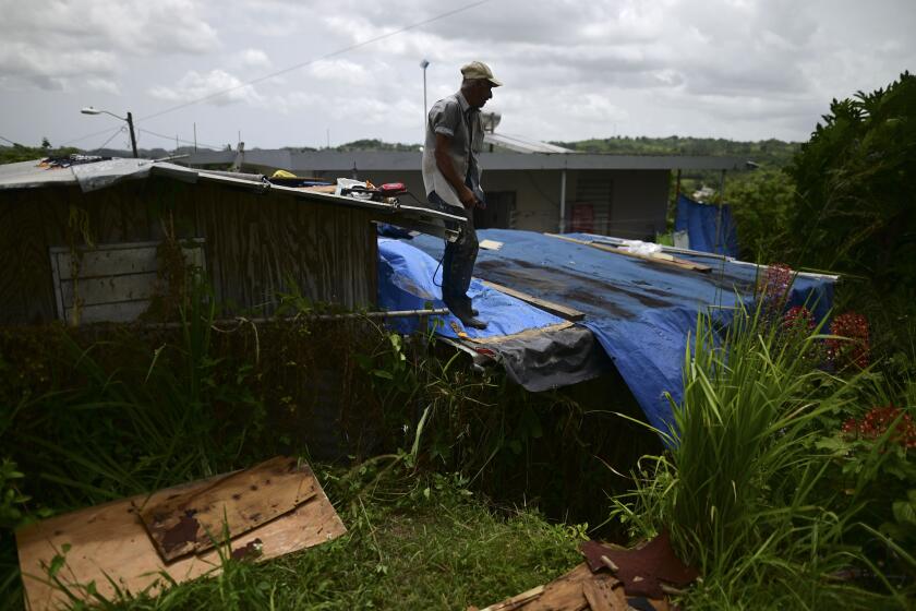 FILE - Wilfredo Negron stands on the rooftop of one of his properties securing the zinc roof in preparation for the current hurricane season on July 13, 2020, in Corozal, Puerto Rico. Five years after Hurricane Maria slammed into Puerto Rico and exposed the funding problems the Caribbean island has long faced, philanthropists warn that many of those issues remain unaddressed, just like the repairs still needed for the American territory’s physical infrastructure. (AP Photo/Carlos Giusti, File)
