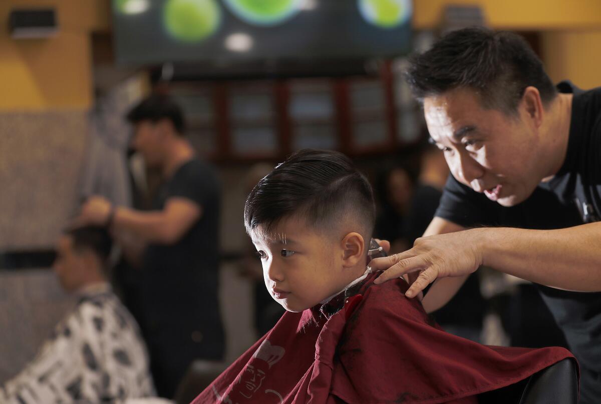 Co-owner Steven Tang gives young customer Ryder Tcheng a haircut at Vinh Hair Salon on West Valley Boulevard in Alhambra.