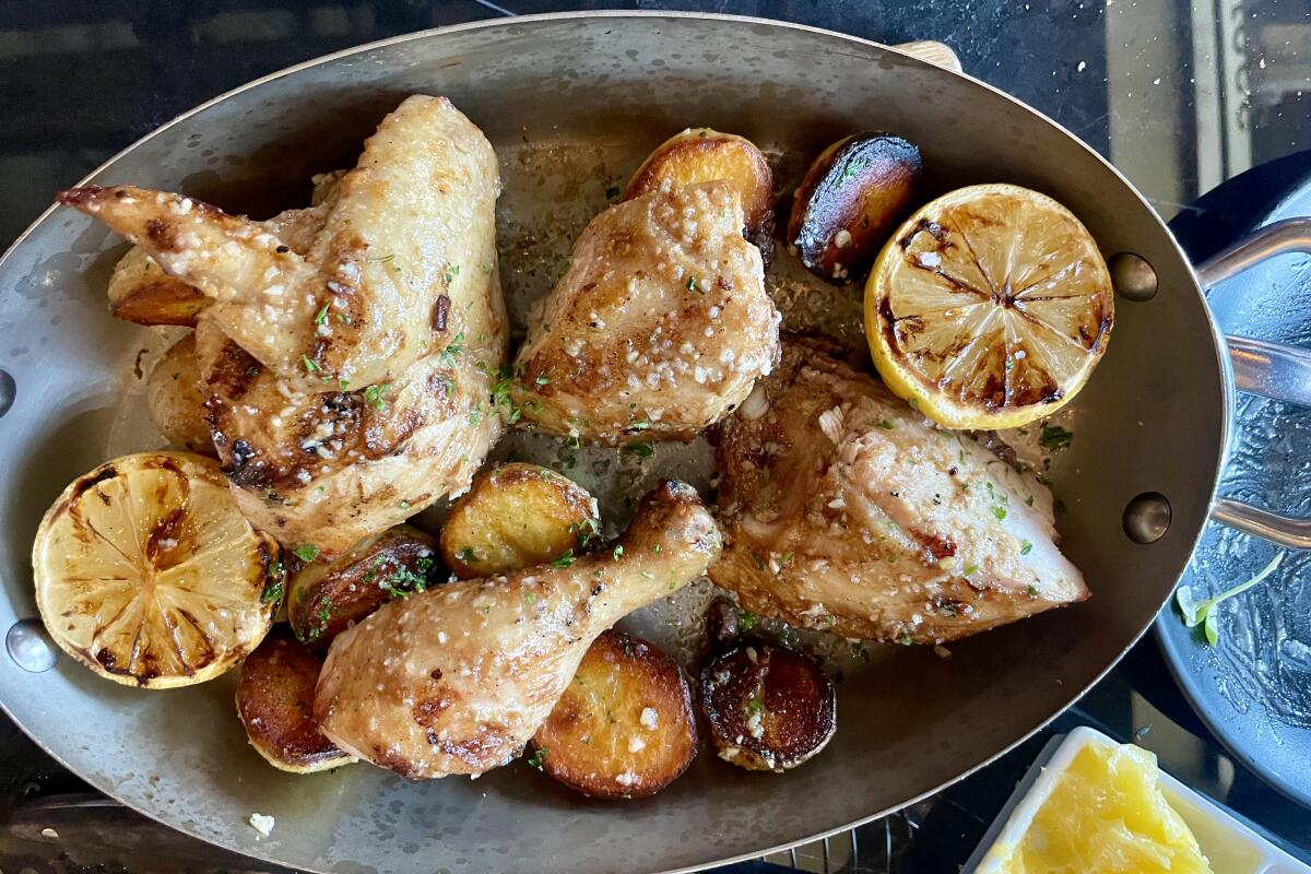 Grilled chicken pieces in an oval dish with grilled lemon halves and potatoes