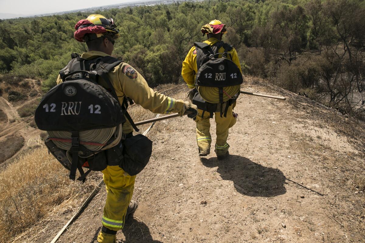 San Bernardino Cal Fire firefighters David Lara, left, and Charles Burks lug extra hose toward the front line near the Prado Dam where firefighters mop up the Prado Fire after it burned more than 1,000 acres over the weekend.