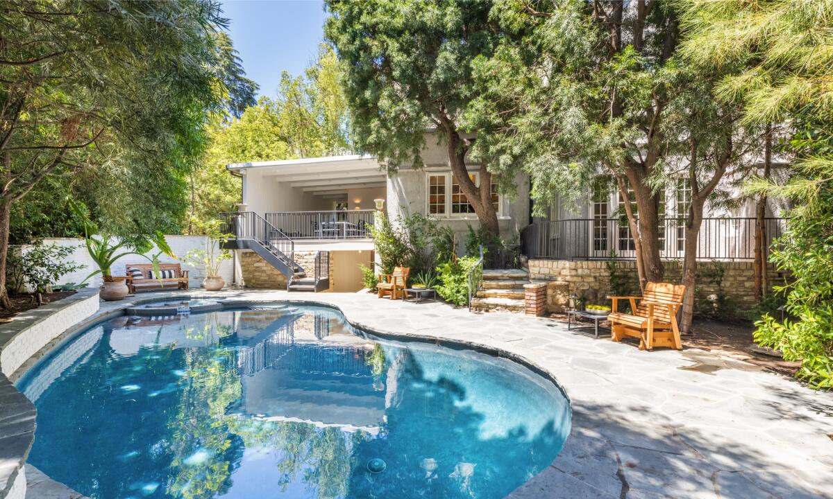 A pool and trees are in front of a home. 