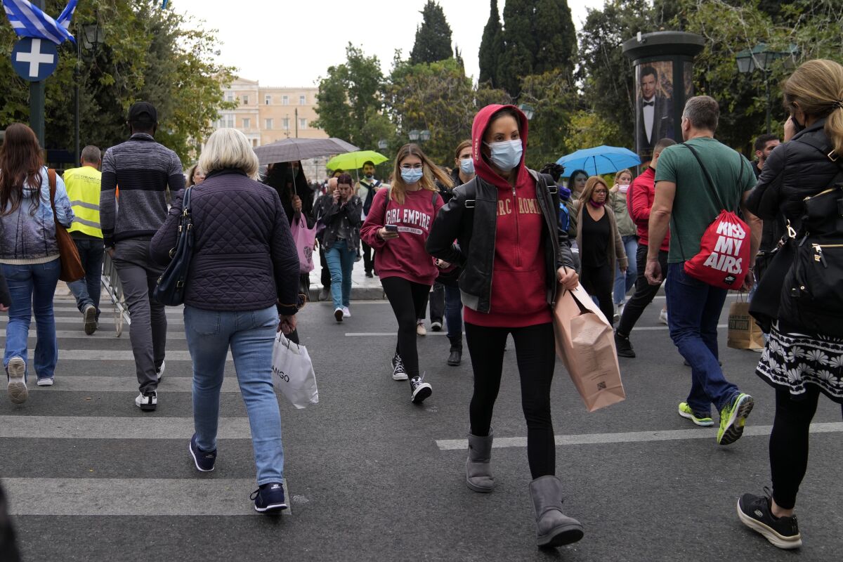 Pedestrians some of them wearing face masks to protect against coronavirus, cross a road at the main Athens' Syntagma square, Greece, Tuesday, Nov. 2, 2021. Greek Health Minister will announce new measures against pandemic after Greece reached new record of daily cases with 5,449 on Monday. (AP Photo/Thanassis Stavrakis)