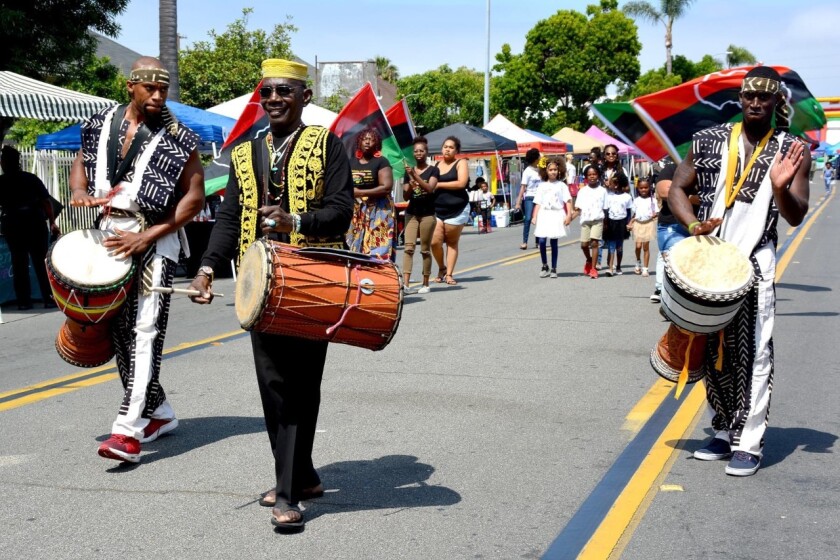 Three men with African drums walk down a city street celebrating.