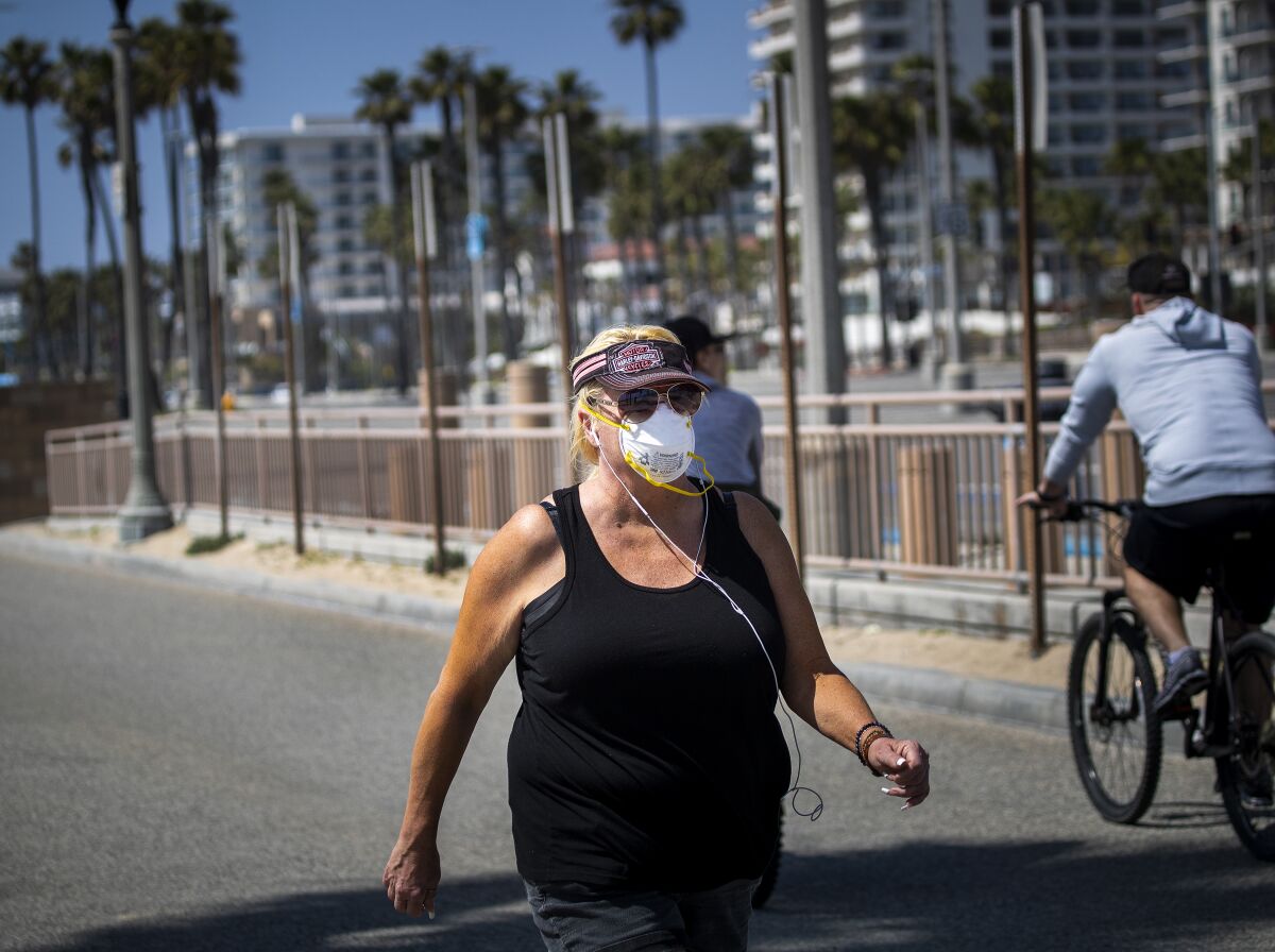 A woman wears a protective mask while exercising on the boardwalk in Huntington Beach
