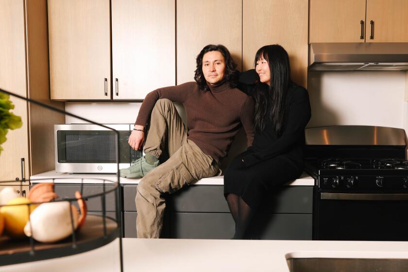 A man and a woman pose together on a countertop in a kitchen with wood cabinets between a stove and a microwave.