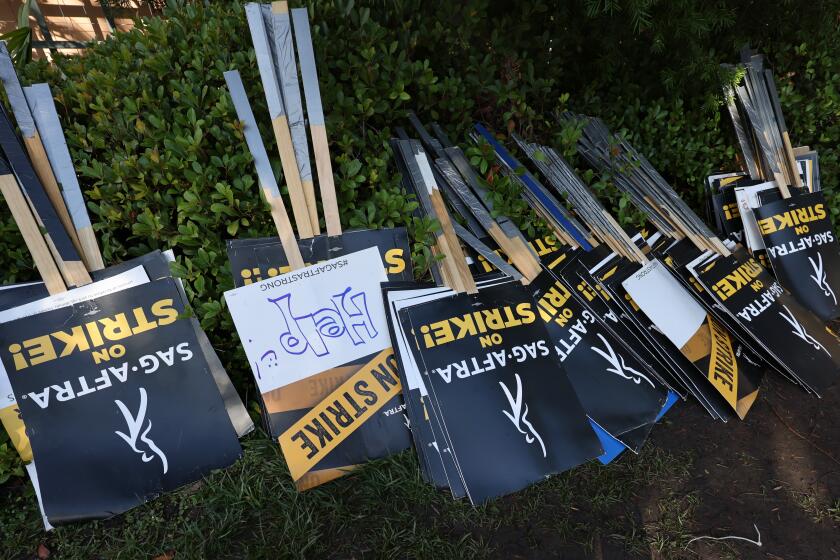 A bunch of SAG-AFTRA picket signs resting upside down against some bushes.