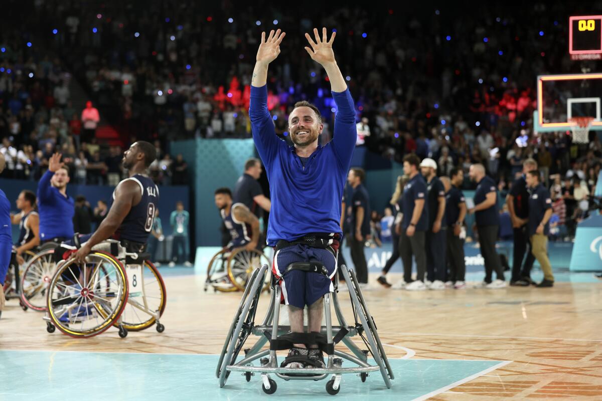 A man in a wheelchair raises his arms in celebration on a basketball court.