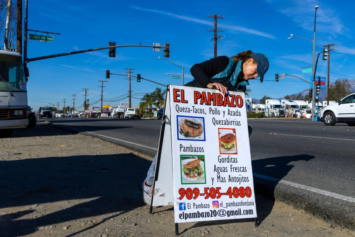 A woman sets up a roadside sign for a food stand. 