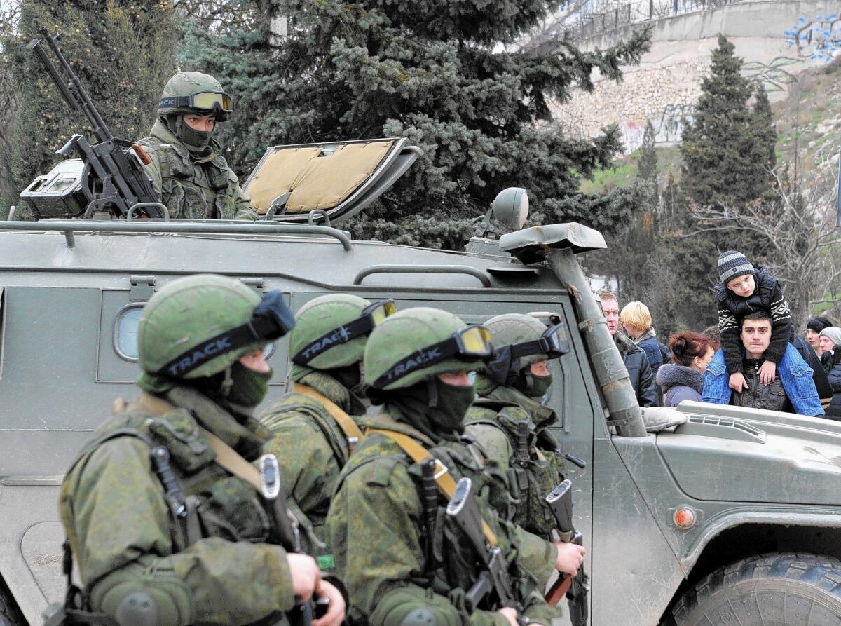 People look at unidentified men in military fatigues blocking a base of the Ukrainian frontier guard unit in Balaklava on Saturday. Ukraine's border guard service said that about 300 armed men were attempting to seize its main headquarters in the Crimean port city of Sevastopol.