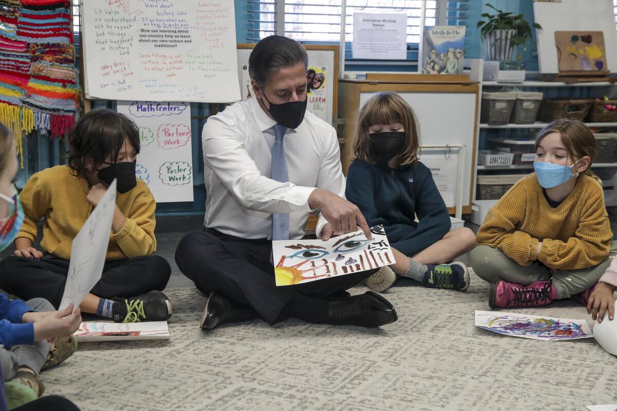 Superintendent Alberto Carvalho sits on the floor with students, showing them a drawing featuring a pair of  eyes and the sun