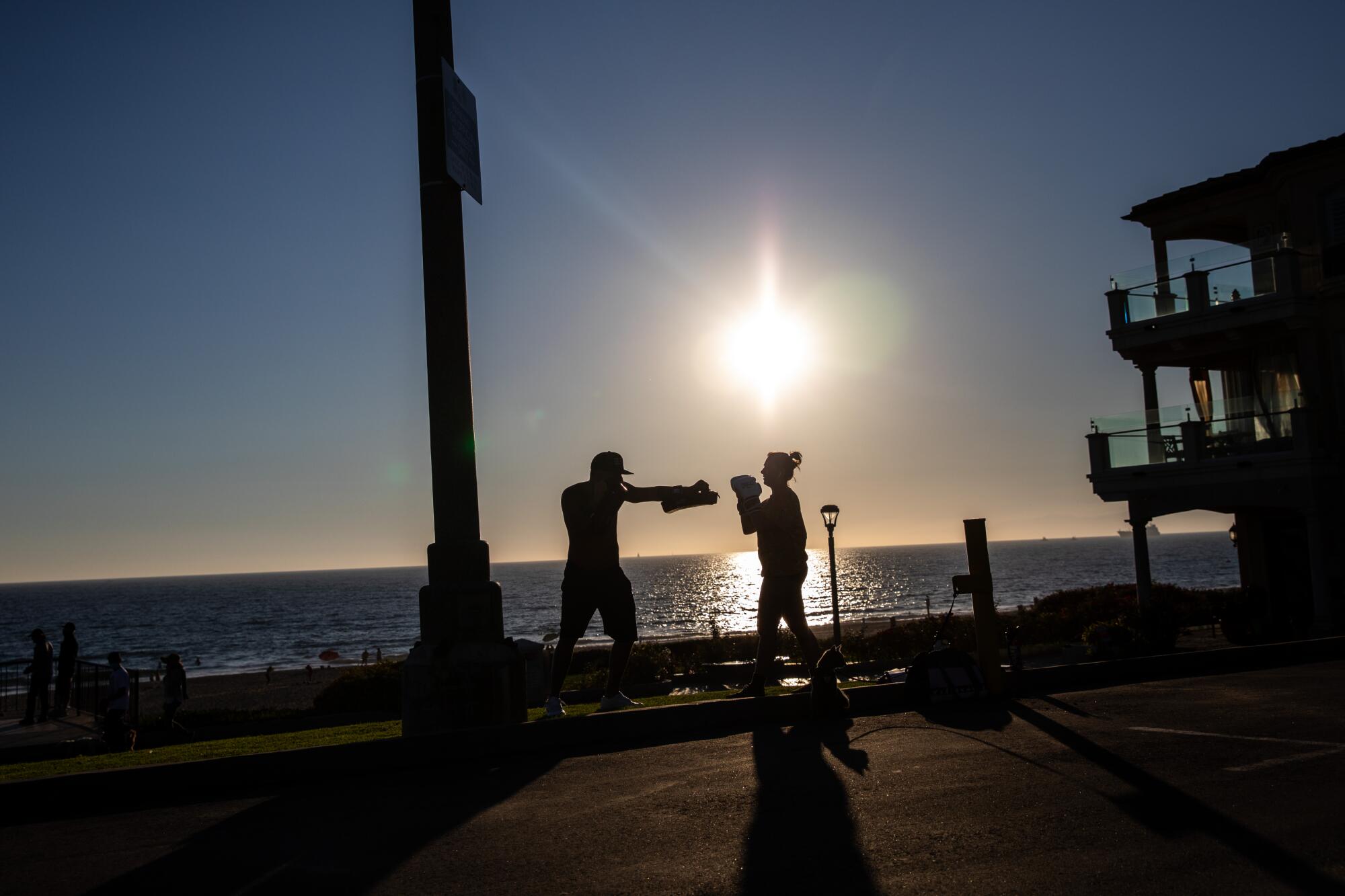 Two people are silhouetted as they work out with boxing gear on Manhattan Beach