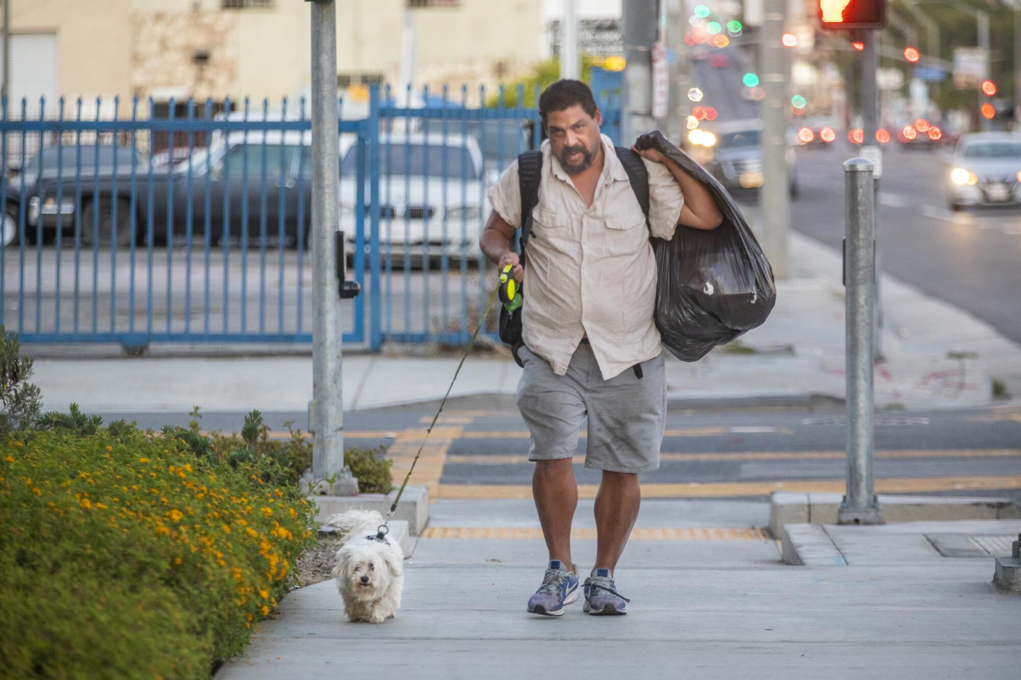 A man walks with a dog and carries a garbage bag