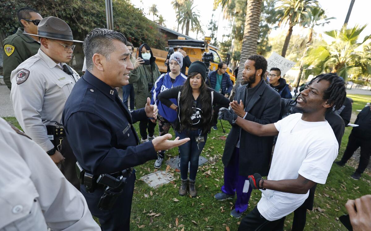 Los Angeles Police Captain Alfonso Lopez, left, talks with camp residents Davone Brown, left and Jhondell Harris, right, as activists are protesting Friday morning at Echo Park Lake, arguing that homeless people should be able to continue camping out at the park as Parks and Recreation workers try to clean the park area which contains tents of a homeless encampment.