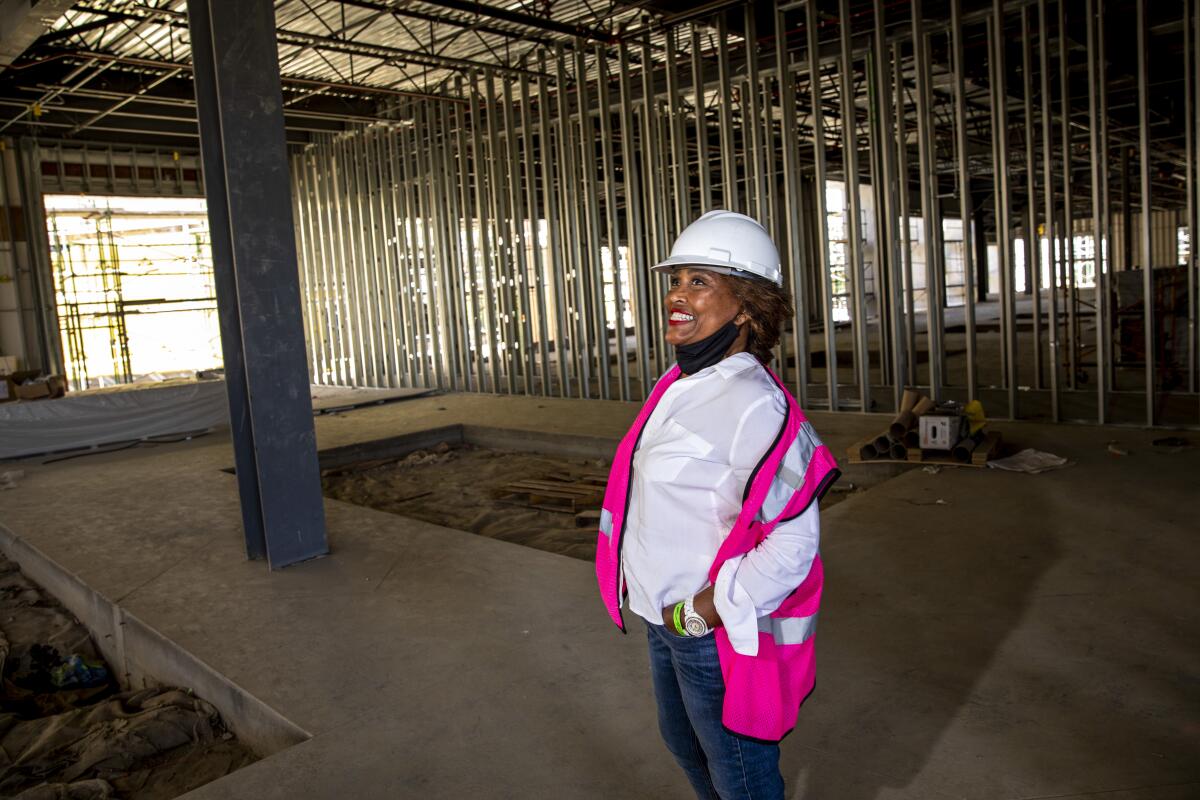 A woman wearing a hard hat smiles while standing in a building under construction.