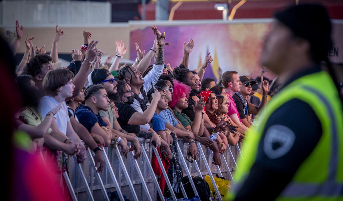 Security keeps an eye on music fans huddled against a barricade.