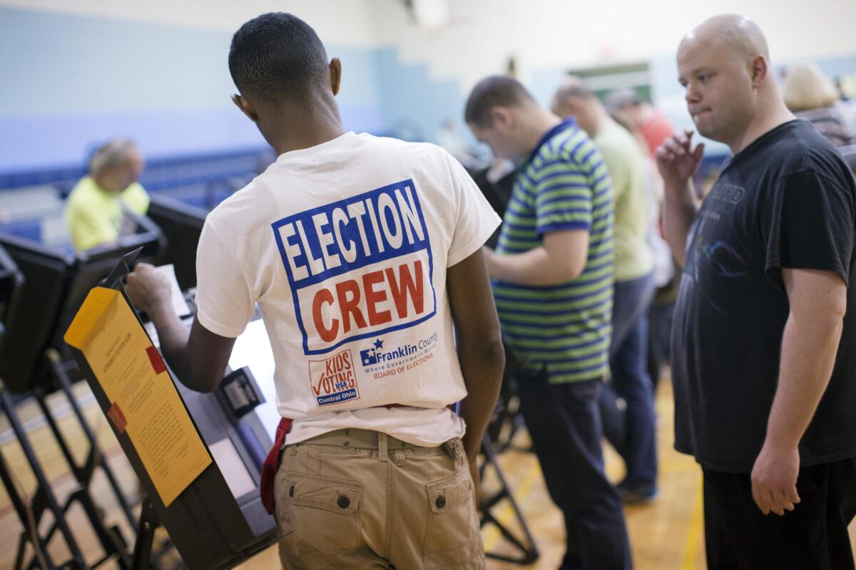 Trayvon Thompson, 17, left, helps a voter use an electronic voting machine at the Schiller Recreation Center polling station Tuesday in Columbus, Ohio. Voters in Ohio are deciding whether to legalize the recreational use of marijuana.