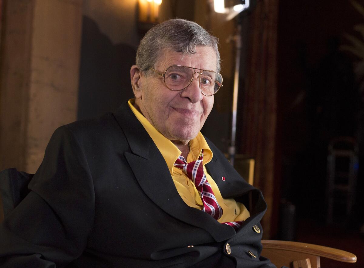 Jerry Lewis smiles at the camera in a blazer and loosened tie