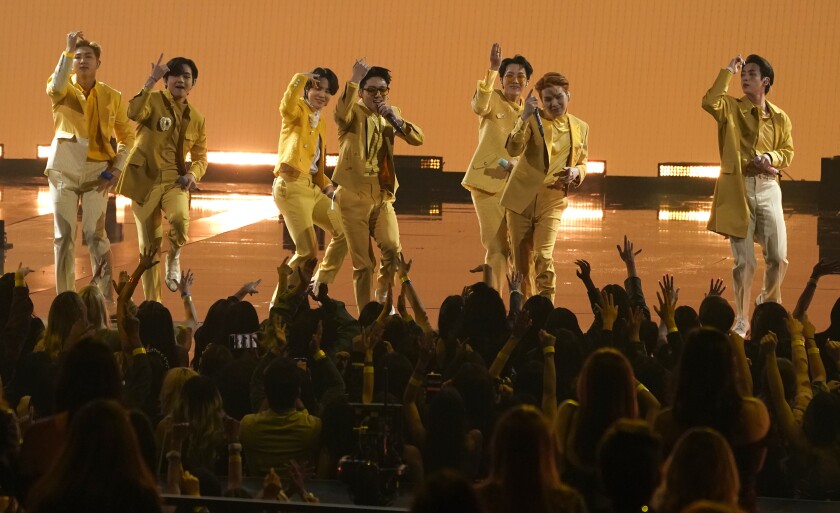 Seven men dance on a stage in yellow suits.