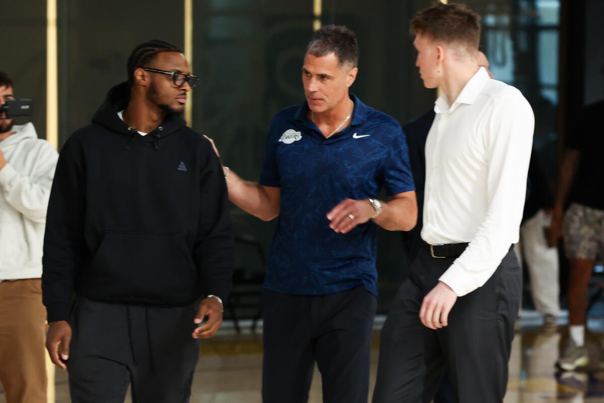 Lakers GM Rob Pelinka, center, talks to Bronny James, left, as they walk toward the podium with Dallas Knecht on Tuesday.