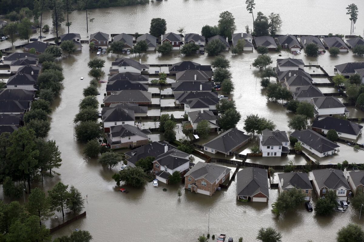 FILE - Homes are surrounded by floodwaters from Tropical Storm Harvey in Spring, Texas, Tuesday, Aug. 29, 2017. Experts say more intense storms driven by climate change are boosting contamination risks for privately-owned drinking water wells. (AP Photo/David J. Phillip, File)