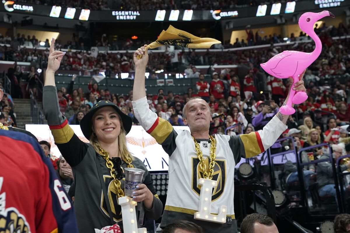 Dos personas con camisetas de hockey de los Golden Knights animan, una sosteniendo un flamenco de plástico