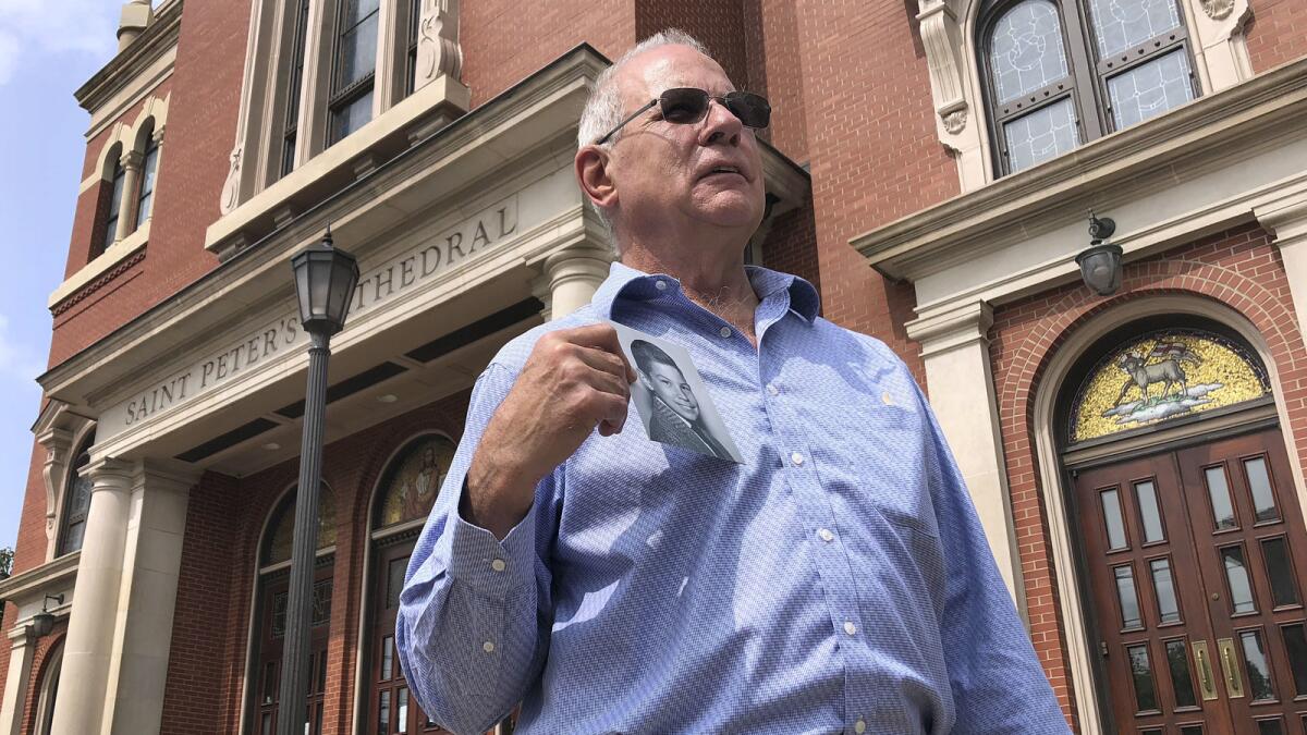 Tim Lennon, president of the Survivors Network of those Abused by Priests, holds a photo of himself as a young boy. Behind him is St. Peter's Cathedral in Scranton, Pa.